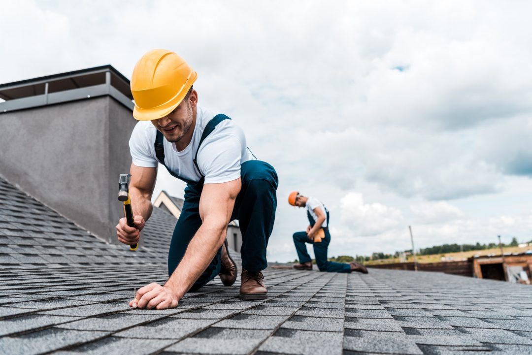 A roofer is repairing roof by using hammer and nail