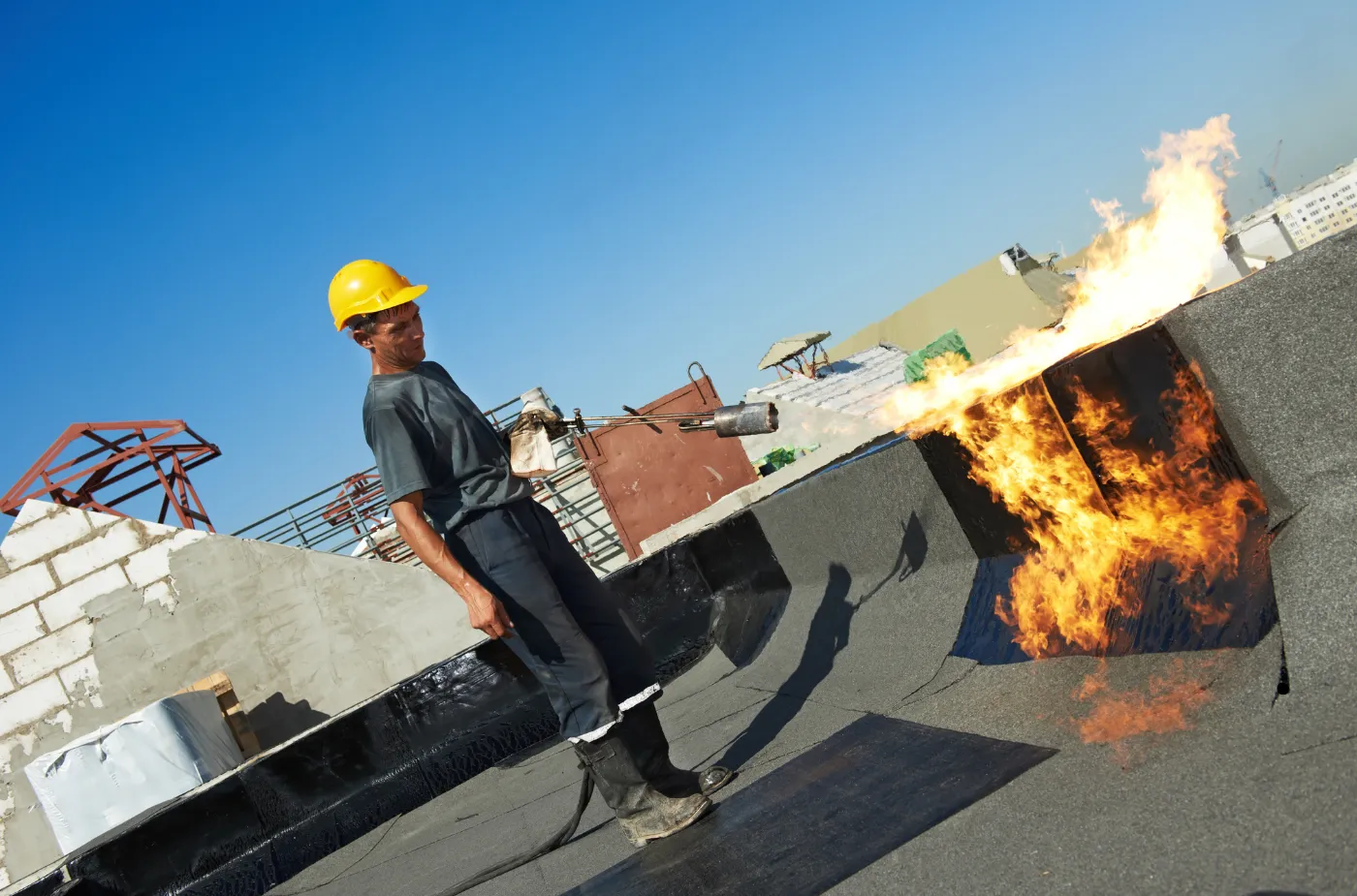 Worker using blowtorch to apply roofing material on a building.