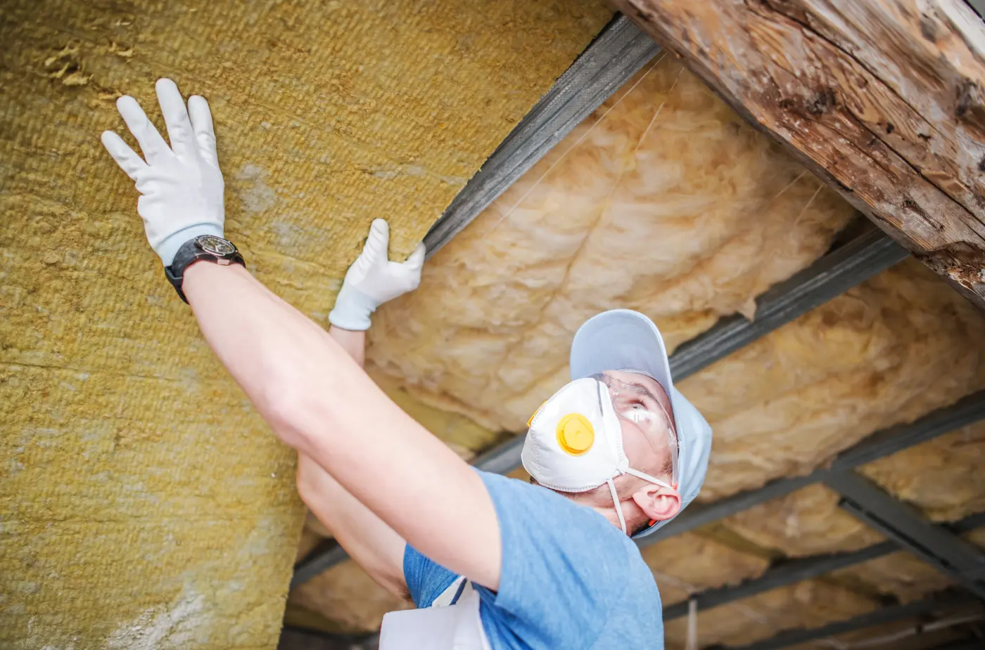 Worker wearing mask and gloves installing insulation under a roof.