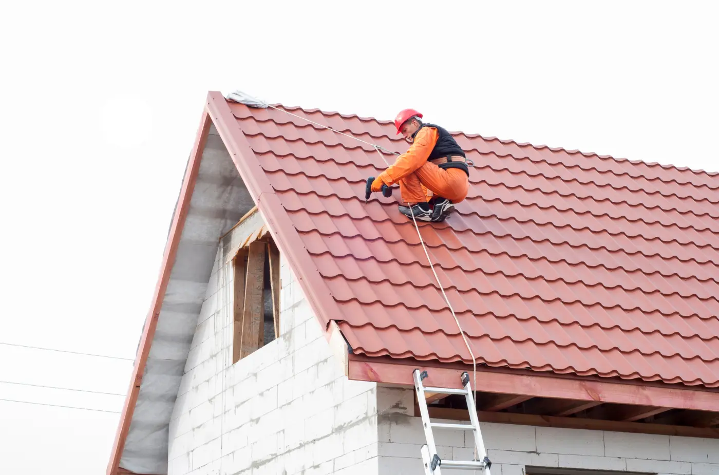 A roofer wearing red helmet and orange suite using drill machine