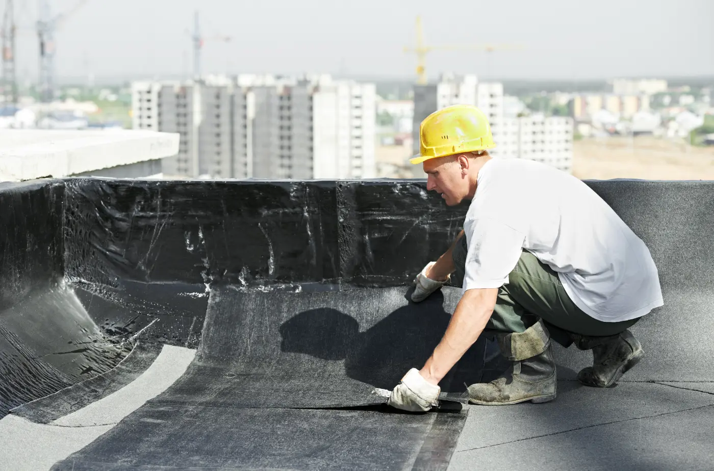 A worker wearing yellow helmet and white t-shirt applying material on roof