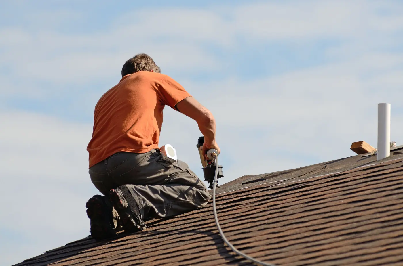 A roofer wearing orange t shirt using drill machine