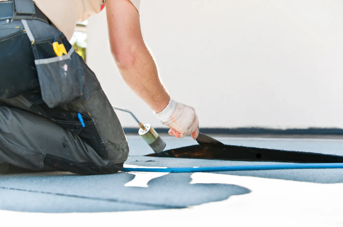 Worker using blowtorch to apply roofing material on a building.