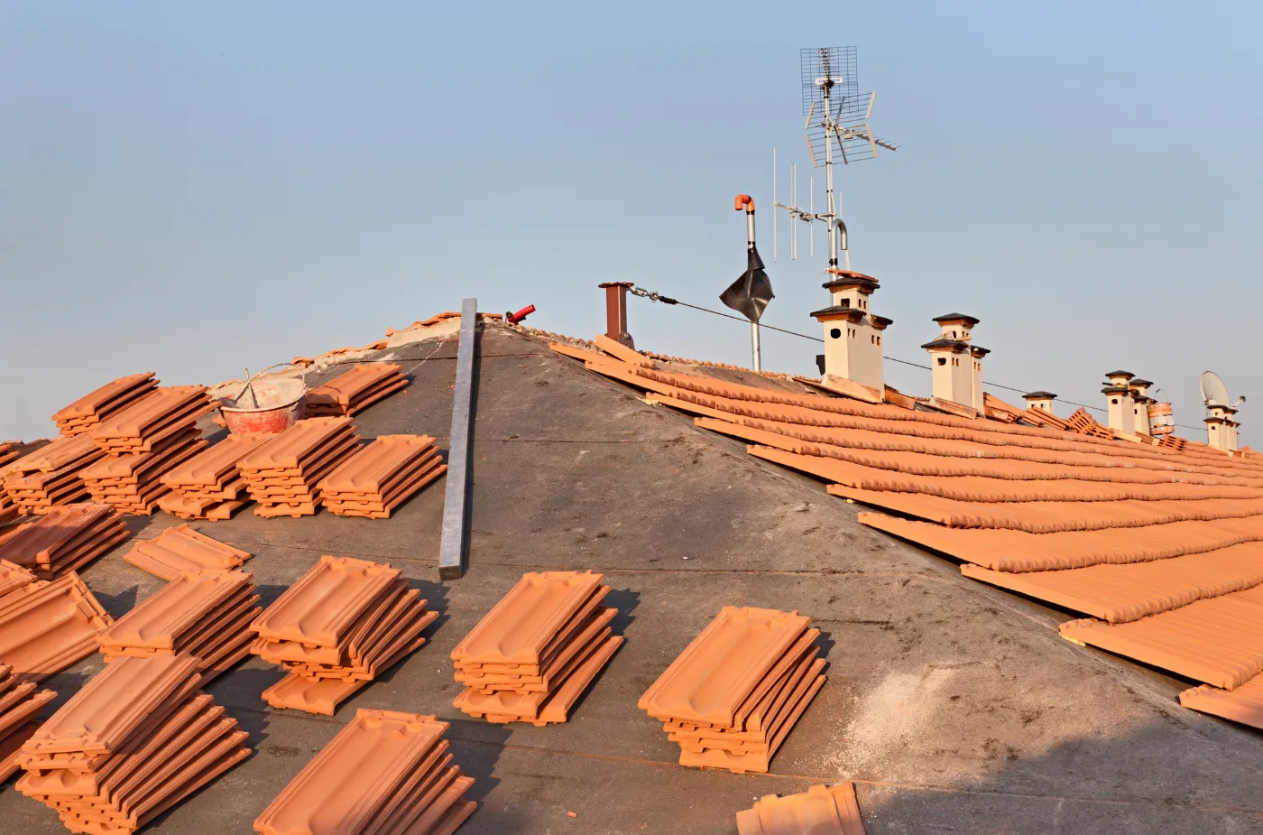 A roof is half covered with red tiles