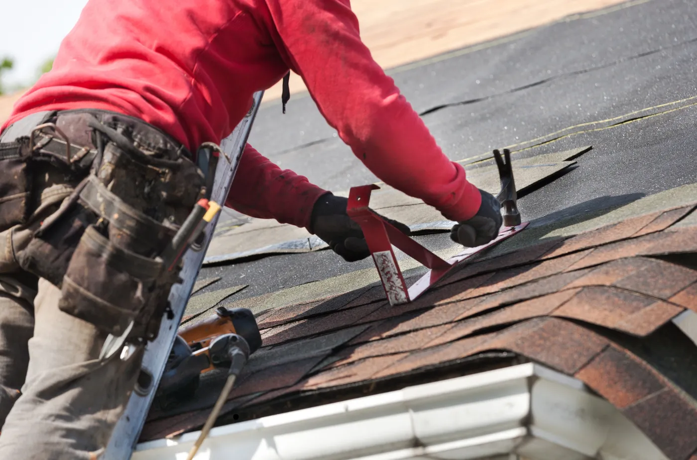 A roofer wearing red jacket is fixing shingles by nail and hammer