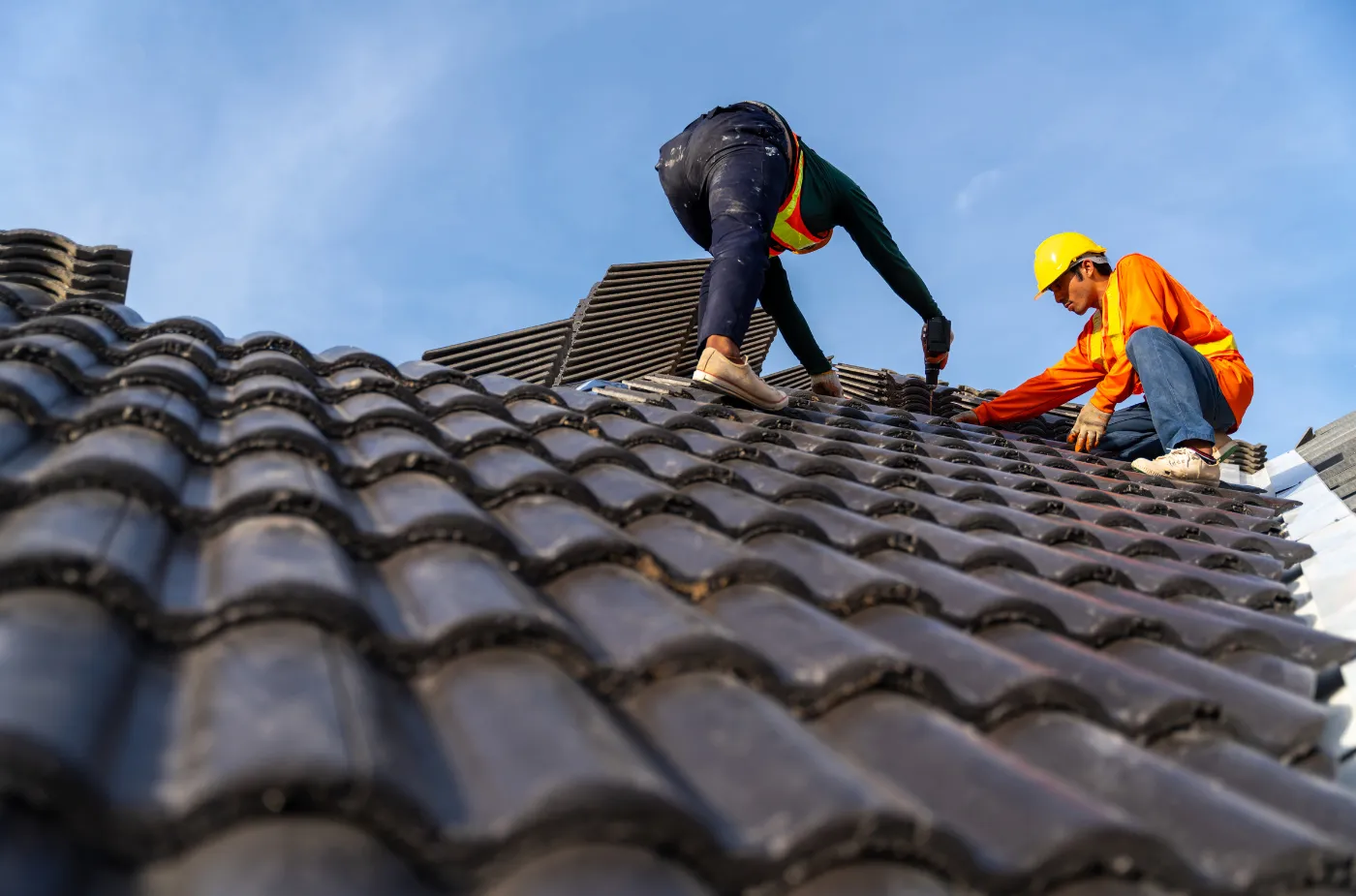 A roofer is fixing black tiles with help of drill machine