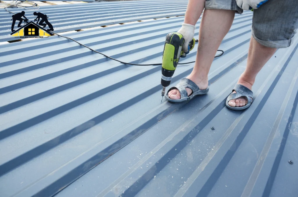 A worker standing on a metal roof while using a power drill to fasten the panels.