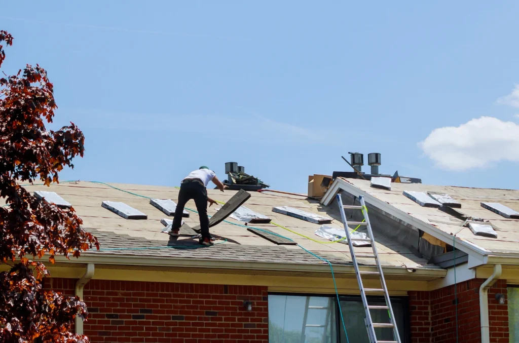 Roofers standing on a sloped roof installing shingles with tools and ladders.