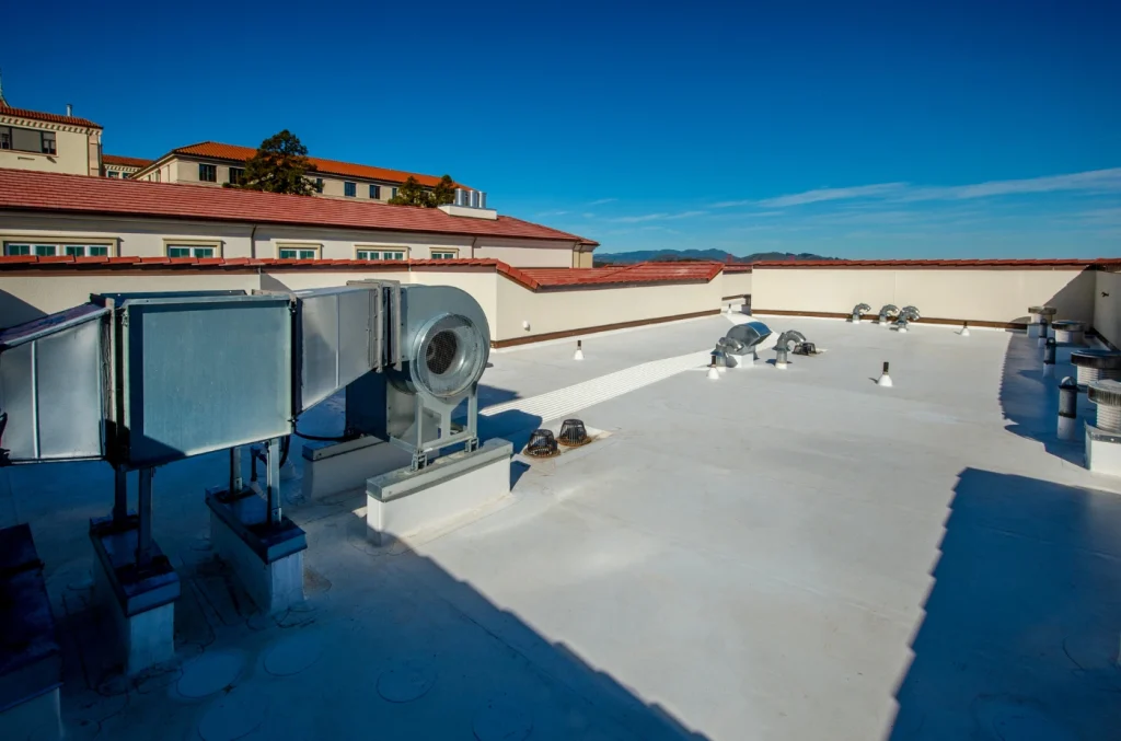arge flat commercial roof covered with white roofing material and HVAC units under a clear blue sky.