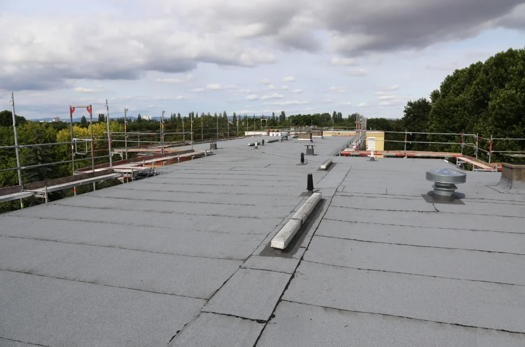 A flat commercial roof covered with rolled roofing membrane under a cloudy sky.