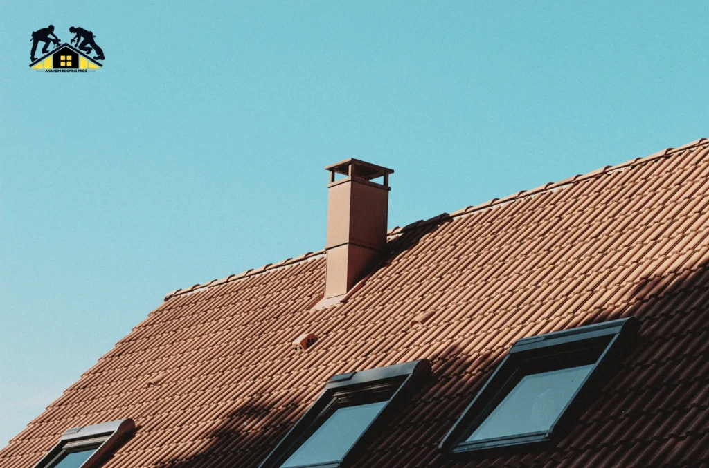 Close-up view of a house roof with reddish-brown tiles under a clear blue sky.