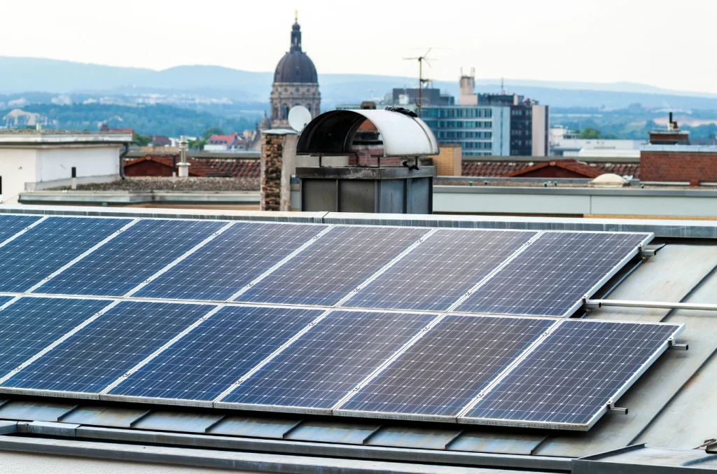 Array of rooftop solar panels with a city skyline and mountains in the background.