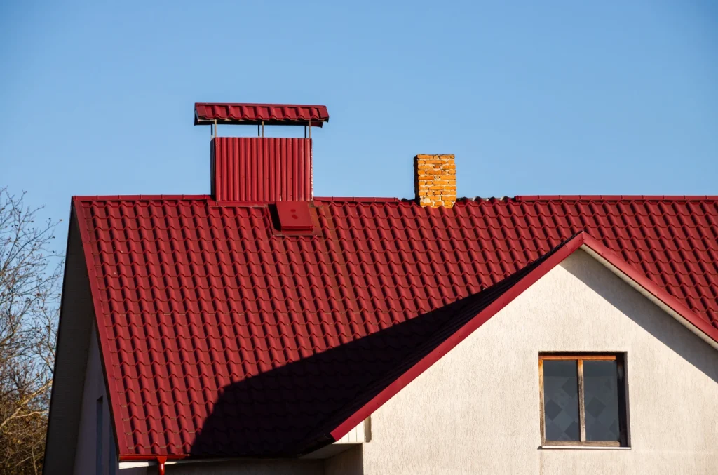 A house with a red metal roof and white exterior walls under a clear sky.