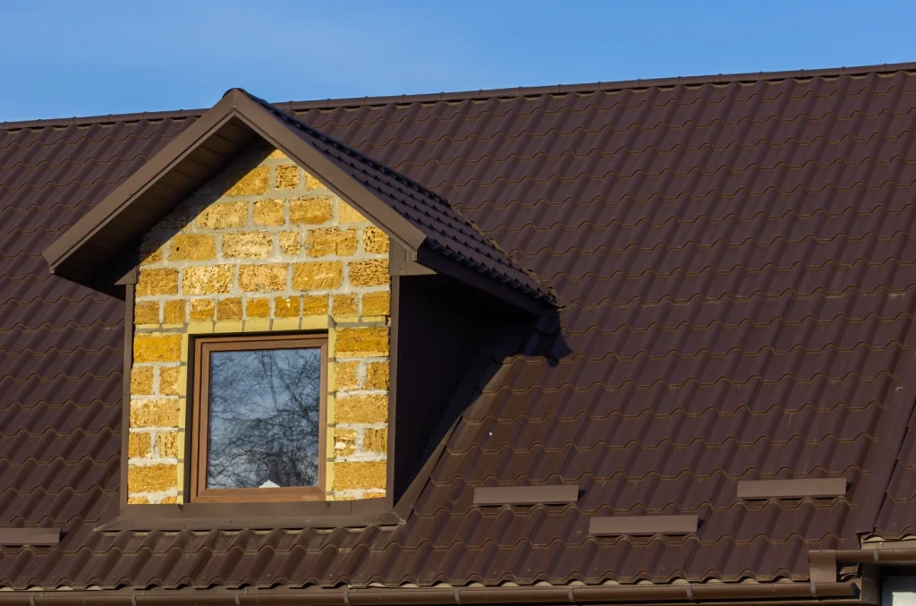 A home featuring a dark brown metal roof with a dormer window and partially finished exterior siding.